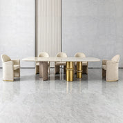 Bodrum Dining Room Table shown with beige upholstered chairs, a light marble tabletop, and gold pedestal bases.