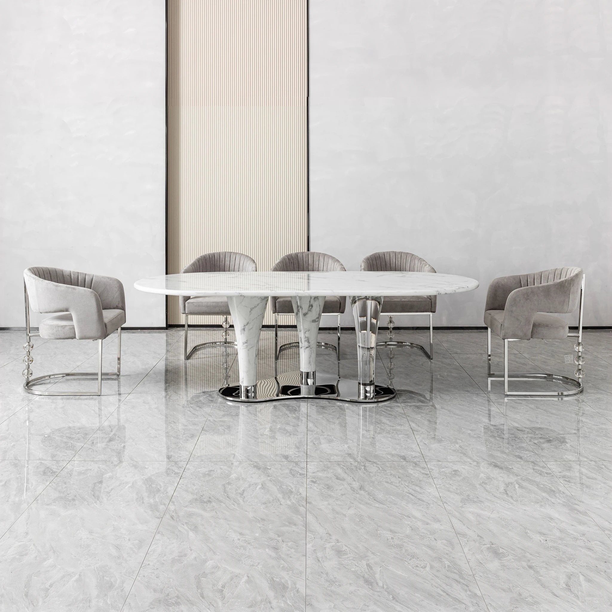 Cristallo dining room table with round white marble top and polished metal pedestal base, surrounded by grey velvet chairs.