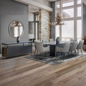 Sierra dining room table with a dark base and glass top, surrounded by light gray upholstered chairs in a modern dining room.